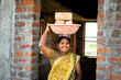 hardworking Indian smiling women with bricks on head looking at camera - concept of daily wagers lifestyle, positive emotional and woman empowerment.