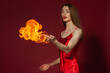 © Roman Kornev - A young woman with long brown hair, in a red dress on a red background with fire