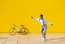 Happy Young Man Dancing In Front Of Yellow Wall On Sunny Day