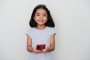 Wall Mural - Asian little girl smiling to the camera while holding a mobile phone
