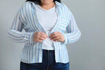 Wall Mural - Overweight woman trying to button up tight shirt on light grey background, closeup