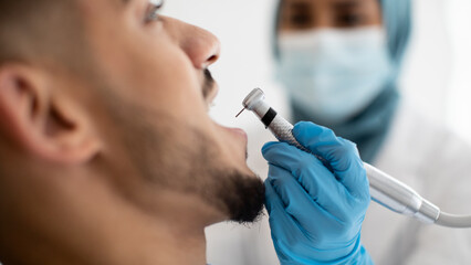 Wall Mural - Muslim Female Dentist Using Dental Drill For Male Patient's Teeth Treatment