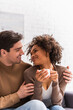 © LIGHTFIELD STUDIOS - Positive african american woman with cup of coffee looking at boyfriend at home