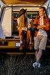 Attractive young couple sit on van from back and have talk, drinking tea after trip, travel, in countryside field. casually dressed man and woman spending good time together