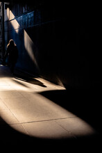 A Silhouette Of A Backlit Lady Walking Though A Passageway With Interesting Shadows.