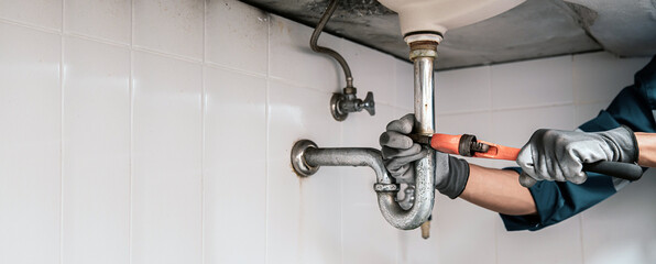 Wall Mural - Technician plumber using a wrench to repair a water pipe under the sink. Concept of maintenance, fix water plumbing leaks, replace the kitchen sink drain, cleaning clogged pipes is dirty or rusty.