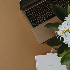Wall Mural - Aesthetic home office desk workspace. Laptop computer, notebook, daisy flowers bouquet in vase on neutral tan brown table. Influencer lifestyle blog background with copy space