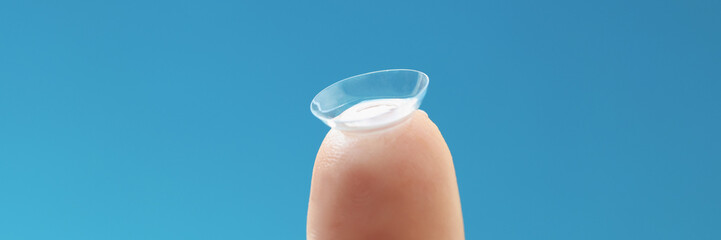 Wall Mural - Soft contact lens on female finger on blue background