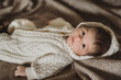 A portrait of little newborn in white cozy knitted overall laying on beige woollen plaid