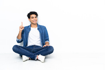 Venezuelan man sitting on the floor showing and lifting a finger in sign of the best