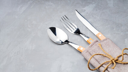 Cutlery on a gray background. Spoon, fork and knife in a linen napkin tied with twine. Table setting. Copy space