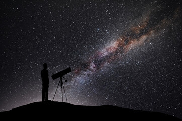 Wall Mural - The silhouette of a man with a telescsope stands on a hill in the starry night sky. Astronomer watching  the milkyway galaxy.