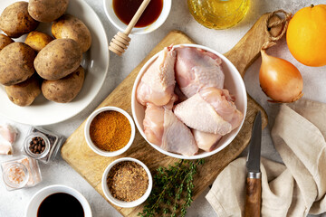 Wall Mural - Raw chicken legs, potatoes and spices on a light gray culinary background. Raw poultry meat, vegetables and seasonings are prepared for pickling. Top view