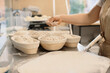 © dsheremeta - Baker woman sprinkles flour on the shaped loaves, rustic style, bread before baking, rustic whole grain bread.