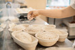 © dsheremeta - Baker woman sprinkles flour on the shaped loaves, rustic style, bread before baking, rustic whole grain bread.