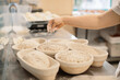 © dsheremeta - Baker woman sprinkles flour on the shaped loaves, rustic style, bread before baking, rustic whole grain bread.