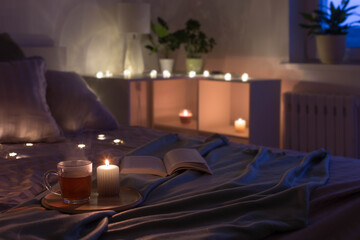 Wall Mural - cup of tea with burning candle on wooden tray on bed in bedroom in evening