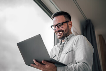 Wall Mural - portrait of young adult smiling cheerful businessman entrepreneur in office using laptop computer ha