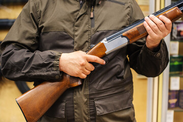 A man holds a shotgun in his hands, finger on the trigger. Double-barreled firearms for bird hunting and sport competitions. Close-up. unrecognizable person