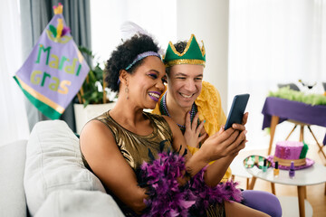 carefree multi-ethnic friends use smart phone during mardi gras party at home.