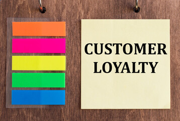 CUSTOMER LOYALTY tex on a yellow card on a wooden background next to colored stickers, business concept