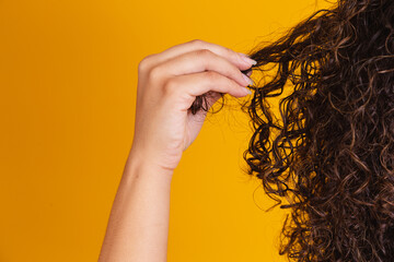 Close-up American African woman pulling a lock of hair. Curly hair on yellow background.