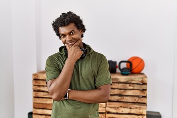 Sticker - African man with curly hair wearing sportswear at the gym looking confident at the camera with smile with crossed arms and hand raised on chin. thinking positive.