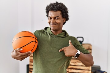 Poster - African man with curly hair holding basketball ball at the gym pointing finger to one self smiling happy and proud