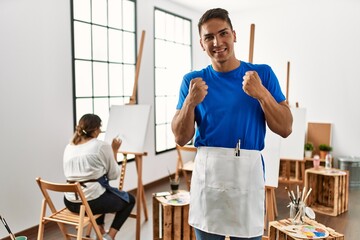 Canvas Print - Young hispanic couple at art studio very happy and excited doing winner gesture with arms raised, smiling and screaming for success. celebration concept.