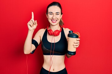 Poster - Young hispanic girl wearing sport clothes drinking a protein shake smiling with an idea or question pointing finger with happy face, number one