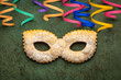 Carnival concept. Traditional italian festive pastry chiacchiere or sfrappole made in a Mask shape and powdered with sugar, decorated with colorful paper serpentine. Dark green background.