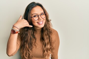 Wall Mural - Young hispanic girl wearing casual clothes and glasses smiling doing phone gesture with hand and fingers like talking on the telephone. communicating concepts.