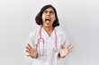 © Krakenimages.com - Young hispanic doctor woman wearing stethoscope over isolated background crazy and mad shouting and yelling with aggressive expression and arms raised. frustration concept.