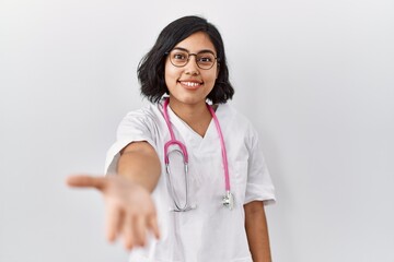 Wall Mural - Young hispanic doctor woman wearing stethoscope over isolated background smiling friendly offering handshake as greeting and welcoming. successful business.