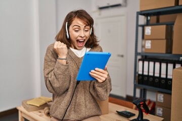 Wall Mural - Young beautiful woman working at small business ecommerce screaming proud, celebrating victory and success very excited with raised arms