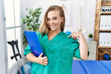 Sticker - Young caucasian woman working at pain recovery clinic looking confident with smile on face, pointing oneself with fingers proud and happy.