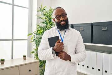 Sticker - Young african american man wearing doctor uniform holding book at clinic