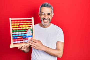 Sticker - Handsome middle age man with grey hair holding traditional abacus looking positive and happy standing and smiling with a confident smile showing teeth