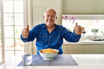 Canvas Print - Senior man with grey hair eating pasta spaghetti at home approving doing positive gesture with hand, thumbs up smiling and happy for success. winner gesture.