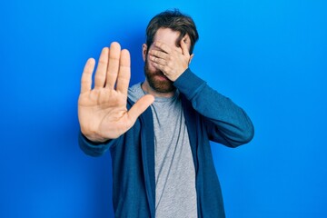 Wall Mural - Caucasian man with beard wearing casual sweatshirt covering eyes with hands and doing stop gesture with sad and fear expression. embarrassed and negative concept.