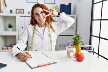 Poster - Young redhead woman nutritionist doctor at the clinic doing peace symbol with fingers over face, smiling cheerful showing victory