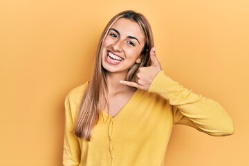 Canvas Print - Beautiful hispanic woman wearing casual yellow sweater smiling doing phone gesture with hand and fingers like talking on the telephone. communicating concepts.