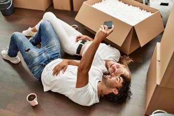 Wall Mural - Young beautiful couple smiling happy making selfie by the smartphone at new home.