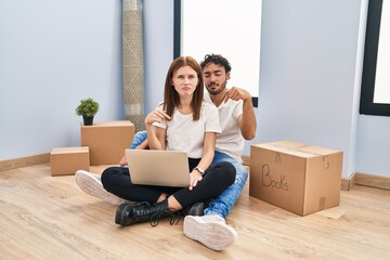 Sticker - Young couple using laptop at new home pointing down looking sad and upset, indicating direction with fingers, unhappy and depressed.