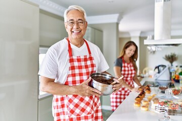 Wall Mural - Middle age hispanic couple wearing apron cooking homemade pastry looking positive and happy standing and smiling with a confident smile showing teeth