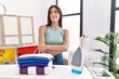 Young hispanic woman ironing clothes at laundry room smiling looking to the side and staring away thinking.