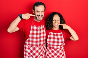 Sticker - Middle age couple of hispanic woman and man wearing cook apron smiling cheerful showing and pointing with fingers teeth and mouth. dental health concept.