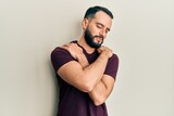 Fototapeta Przeznaczenie - Young man with beard wearing casual t shirt hugging oneself happy and positive, smiling confident. self love and self care