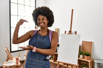 Canvas Print - Young african american woman with afro hair at art studio gesturing with hands showing big and large size sign, measure symbol. smiling looking at the camera. measuring concept.