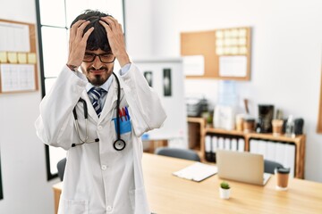 Poster - Hispanic man with beard wearing doctor uniform and stethoscope at the office suffering from headache desperate and stressed because pain and migraine. hands on head.